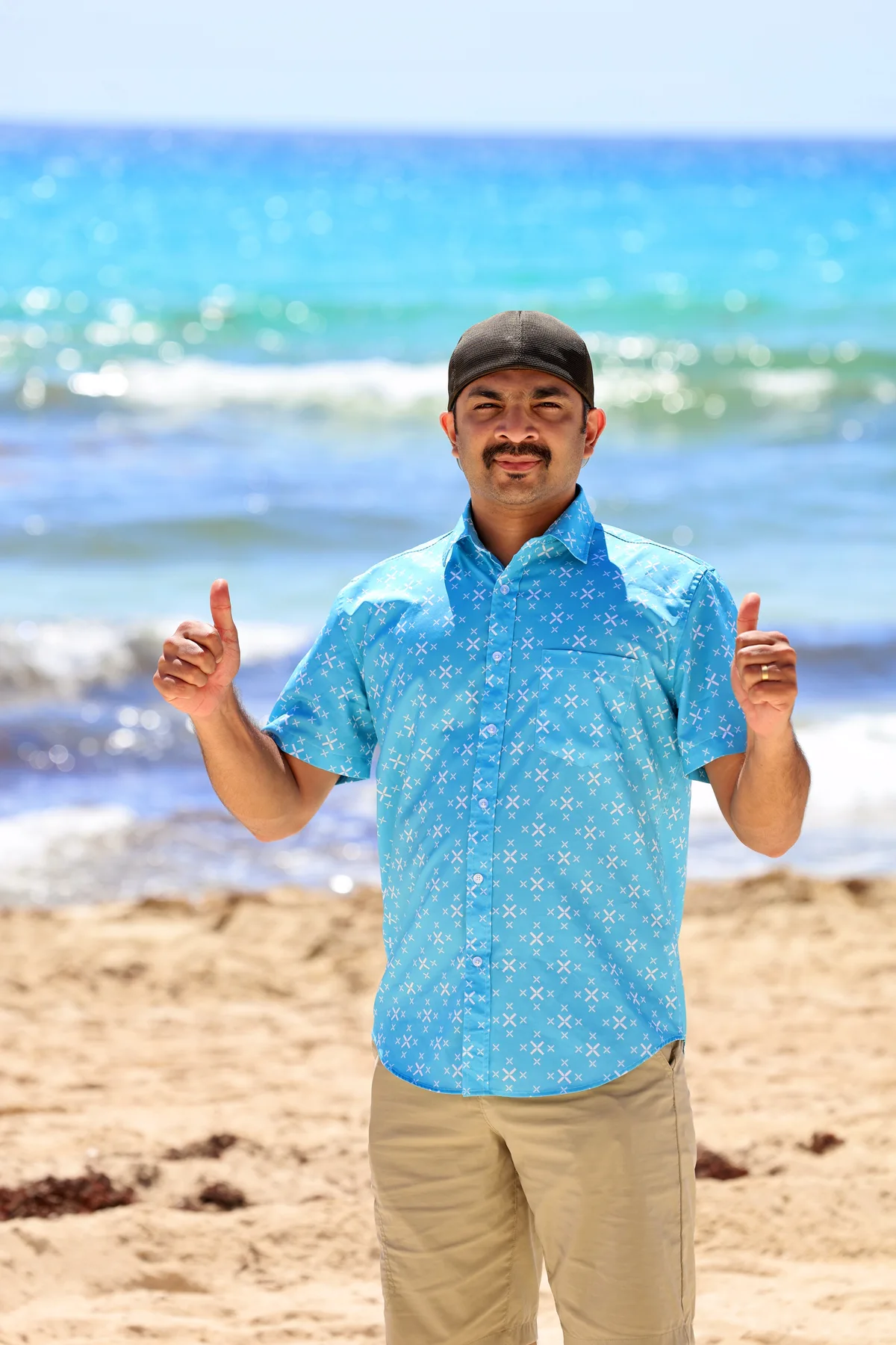 A man in a blue shirt standing on Cancún beach, with turquoise water behind him.