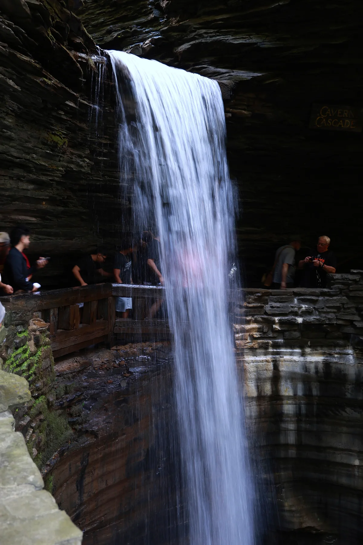 A waterfall beside a stone walkway with visitors at Watkins Glen.